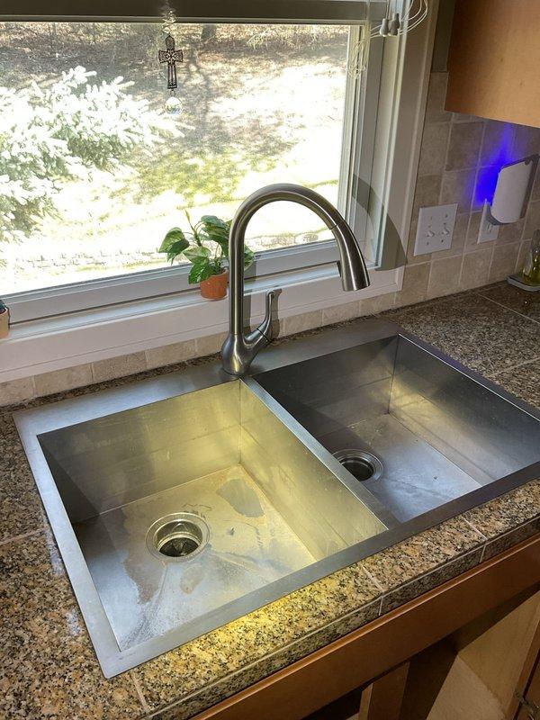 Responded to kitchen sink drainage issue. Upon arrival, found dual-basin stainless steel sink with garbage disposal unit experiencing complete blockage preventing water flow. Inspected under-sink plumbing configuration including black garbage disposal unit, white PVC drain lines, and trap assembly. Cleared obstruction from disposal unit and drain line using appropriate drain cleaning methods. Verified proper drainage flow in both sink basins. Tested garbage disposal operation and confirmed restored functionality. Checked all connections for leaks and verified system integrity before completion.