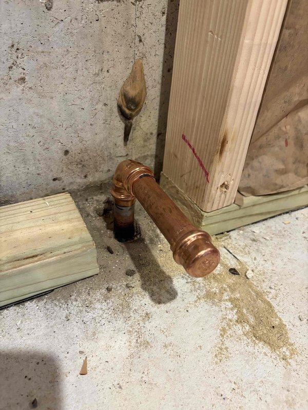 Completed third visit to address persistent leaking at new copper pipe connection caps on 13-year-old Utica boiler system. Previous cap installations continued to leak despite multiple attempts. Inspected copper piping penetration through basement ceiling, assessed elbow joint connections at floor level, and evaluated oxidized copper fittings showing weathered patina. Replaced defective caps with proper fittings to achieve leak-free seal. Verified all connections were secure and tested system for proper operation. Documented installation with photos showing pipe routing through wooden framing and concrete foundation area.