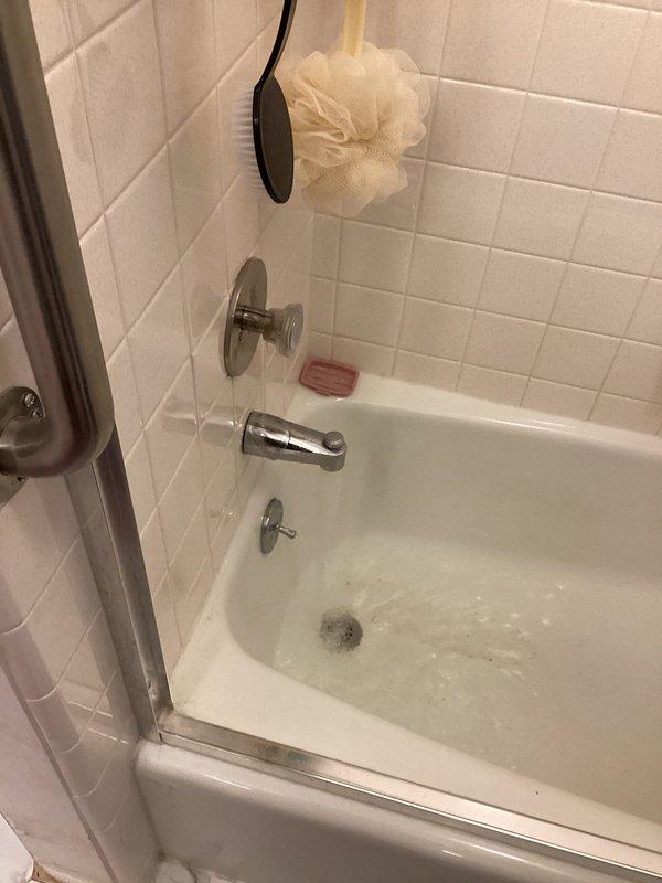 Responded to severely backed-up shower drain in downstairs bathroom of 52-year-old residence with history of intermittent drainage issues. Upon arrival, assessed white subway-tiled shower stall with visible aging, grout discoloration, and rust staining around drain assembly. Cleared complete blockage from shower drain line, restoring full water flow and drainage capacity. Documented existing conditions showing wear consistent with building age, including mineral deposits and surface staining on fixtures and tile surfaces.