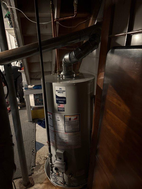 Completed full water heater replacement in basement utility area, removing existing unit and installing new Bradford White natural gas water heater. Connected all copper supply and discharge piping with proper fittings and joints, installed black flexible exhaust venting from top of unit, and verified all connections for proper operation and code compliance. Unit tested successfully with no leaks detected and all safety labels intact.