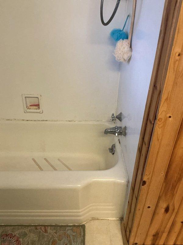 Conducted on-site assessment for bathroom remodel project. Documented existing bathroom conditions including standard beige bathtub with chrome fixtures, wall-mounted shower assembly with flexible hose, and surrounding white-painted walls showing typical moisture-related wear. Photographed current plumbing fixtures, bathtub configuration, and wall conditions to prepare comprehensive project estimate for complete bathroom renovation.