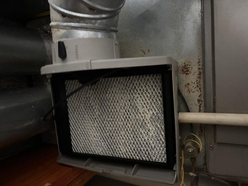 Completed furnace super tune-up on Bryant HVAC system. Inspected air filter housing and found pleated air filter with accumulated dust and debris requiring replacement. Noted visible rust and corrosion on metal housing panel surrounding filter assembly. Examined Zone-A-Trol M8R motor spring return control module with 24 VAC operation, verified wiring connections secured with wire nuts, and confirmed proper installation within air handler unit. Inspected condensate drainage system including white PVC piping and brass valve connections. All accessible components photographed and system operational upon completion of tune-up procedures.