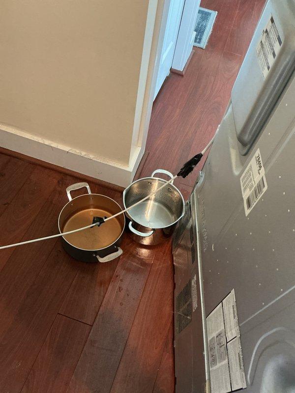 Responded to emergency plumbing leak in basement with water accumulation at approximately half gallon per hour. Upon arrival, found active leak with collection pots positioned on hardwood flooring to catch water. Investigated suspected refrigerator water line as source of leak. Identified and isolated leak source, performed necessary repairs to stop water flow. No dedicated shutoff valve was present at the fixture, requiring main water supply manipulation to complete repairs safely.