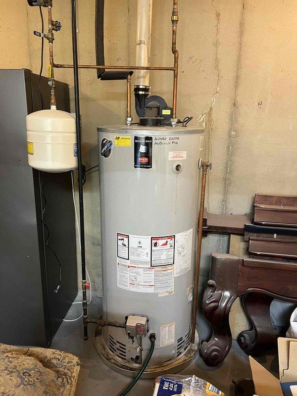 Performed on-site assessment of residential water heater system in basement utility area to provide replacement estimate. Documented existing installation including standard residential water heater with connected expansion tank, copper supply piping, recirculation pump, and PVC drainage system. Photographed current equipment configuration and surrounding plumbing connections for accurate proposal development.