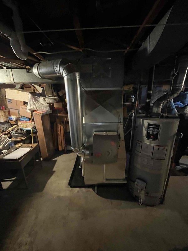 Successfully completed full furnace installation in basement utility area. New gray furnace unit was positioned and secured with metallic exhaust venting installed and routed upward through ceiling joists. All ductwork connections were completed, including plenum attachment and distribution system integration. System was tested for proper operation, airflow verified, and all safety checks performed to ensure code compliance.