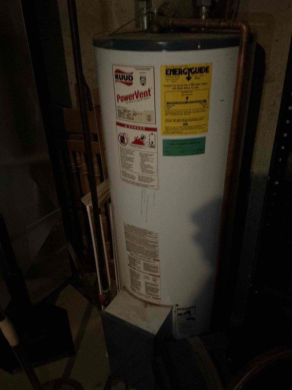 Responded to a basement drainage issue where a PVC drain line connecting to the sewage system had developed a small crack affecting the basement bathroom. Upon arrival, inspected the plumbing configuration in the utility area and identified the compromised section of white PVC drainage piping. Documented the existing drainage system layout, including the vertical and horizontal pipe runs with multiple elbows and joints near the water heater location. Assessed the crack in the PVC drain line and determined the necessary repair to restore proper drainage function and prevent water damage to the basement area.
