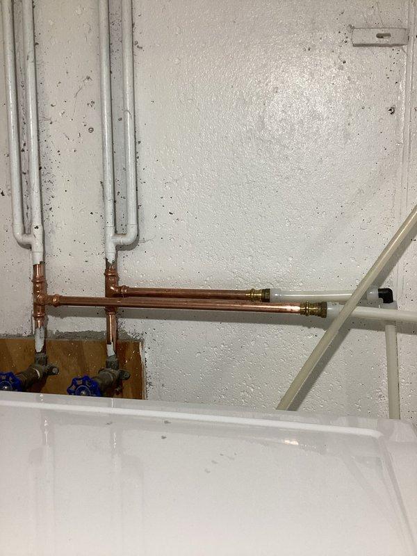 Completed utility sink installation in basement area, including full rough-in and finish plumbing. Installed new water supply lines using copper piping with brass compression fittings and T-joints to create dedicated hot and cold water feeds. Mounted two PVC supply risers with blue-handled shutoff valves for independent water control. Set white utility sink with chrome two-handle faucet and connected to existing drainage system using white PVC waste lines with proper venting and trap configuration. All plumbing connections tested and verified leak-free upon completion.