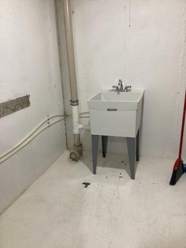 Completed utility sink installation in basement area, including full rough-in and finish plumbing. Installed new water supply lines using copper piping with brass compression fittings and T-joints to create dedicated hot and cold water feeds. Mounted two PVC supply risers with blue-handled shutoff valves for independent water control. Set white utility sink with chrome two-handle faucet and connected to existing drainage system using white PVC waste lines with proper venting and trap configuration. All plumbing connections tested and verified leak-free upon completion.