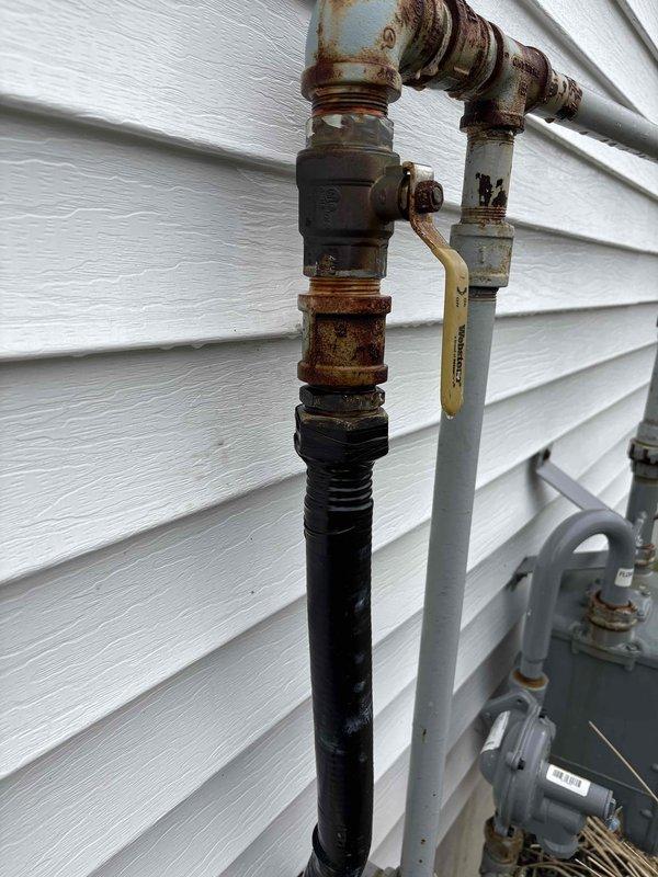 Responded to emergency gas leak on exterior gas line between meter and house. Upon arrival, confirmed utility company had shut off gas supply due to active leak, leaving property without heat or hot water. Conducted thorough inspection of exterior gas piping system and identified significant corrosion and rust at multiple threaded pipe connections, particularly at elbow fittings on the black iron pipe assembly. The deteriorated fittings showed extensive oxidation from prolonged weather exposure, compromising the integrity of the gas line connections. Documented all affected areas with photographs showing corroded brass/bronze fittings and rusted connection points on the vertical and horizontal pipe runs mounted to building exterior. Advised customer of necessary repairs to restore safe gas service to the property.