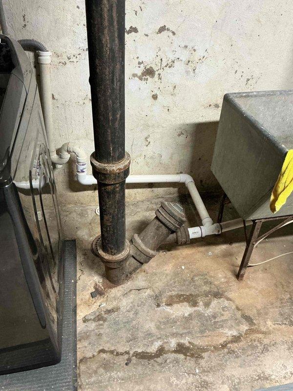 Responded to recurring sewer odor complaint with shower and sink drainage backup issues. Upon inspection, identified severely corroded vertical drain pipe in basement utility area with compromised metal couplings and deteriorated sediment trap assembly. Pipe exhibited extensive rust throughout, indicating advanced age and moisture exposure. Additionally, discovered damaged flexible gas connector line at kitchen range with multiple breach points where outer protective covering had separated, exposing internal reinforcement materials and creating potential safety hazard. Documented all findings with photographic evidence showing extent of corrosion on drainage system and compromised integrity of gas line connector. Advised immediate replacement of both corroded drain piping assembly and damaged gas connector to resolve odor infiltration and prevent potential gas leak situation.