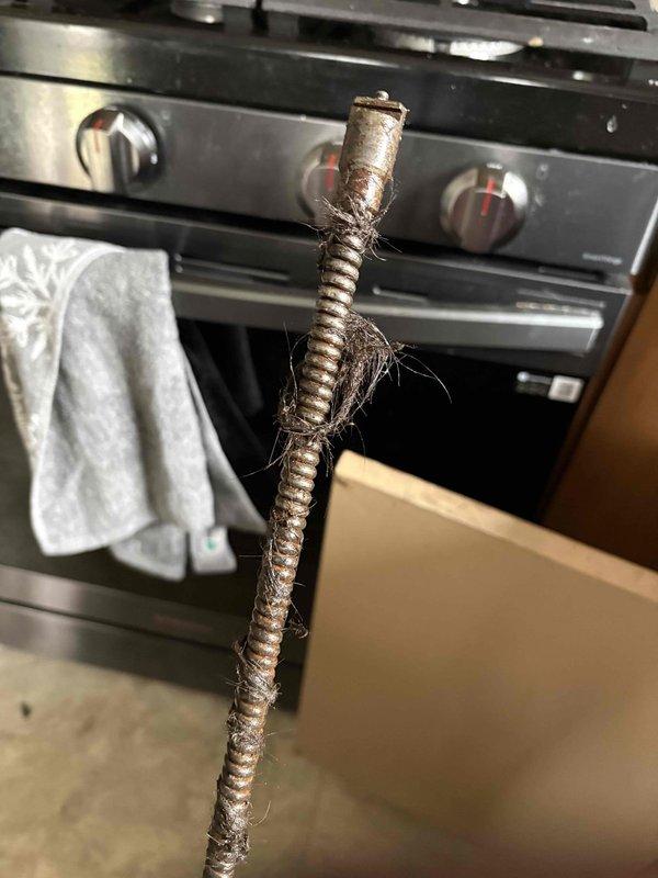 Responded to recurring sewer odor complaint with shower and sink drainage backup issues. Upon inspection, identified severely corroded vertical drain pipe in basement utility area with compromised metal couplings and deteriorated sediment trap assembly. Pipe exhibited extensive rust throughout, indicating advanced age and moisture exposure. Additionally, discovered damaged flexible gas connector line at kitchen range with multiple breach points where outer protective covering had separated, exposing internal reinforcement materials and creating potential safety hazard. Documented all findings with photographic evidence showing extent of corrosion on drainage system and compromised integrity of gas line connector. Advised immediate replacement of both corroded drain piping assembly and damaged gas connector to resolve odor infiltration and prevent potential gas leak situation.