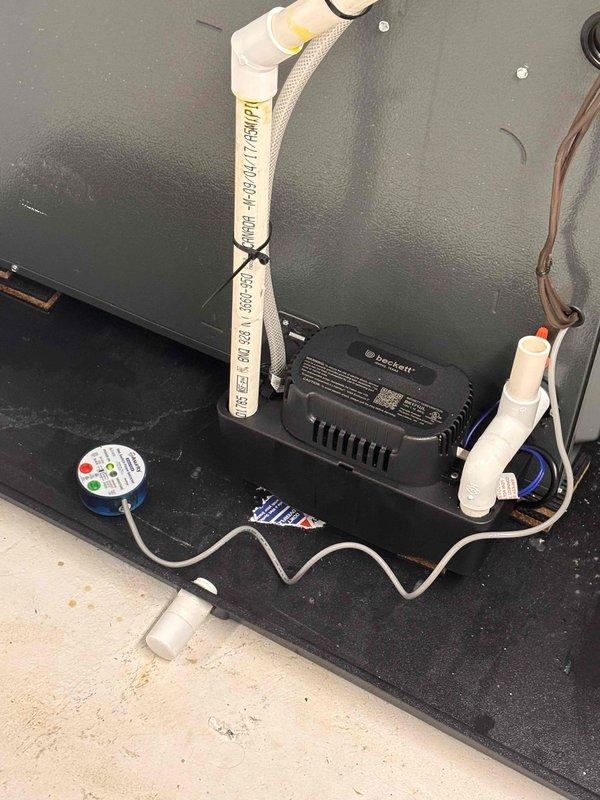 Installed condensate drainage system for refrigeration unit. Added white PVC piping with proper elbow joints and secured condensate line routing using metal hose clamps with adjustment mechanisms. Connected condensate pump with indicator lights and integrated electrical transformer to ensure proper drainage operation and prevent water accumulation issues.