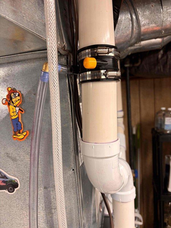 Installed condensate drainage system for refrigeration unit. Added white PVC piping with proper elbow joints and secured condensate line routing using metal hose clamps with adjustment mechanisms. Connected condensate pump with indicator lights and integrated electrical transformer to ensure proper drainage operation and prevent water accumulation issues.