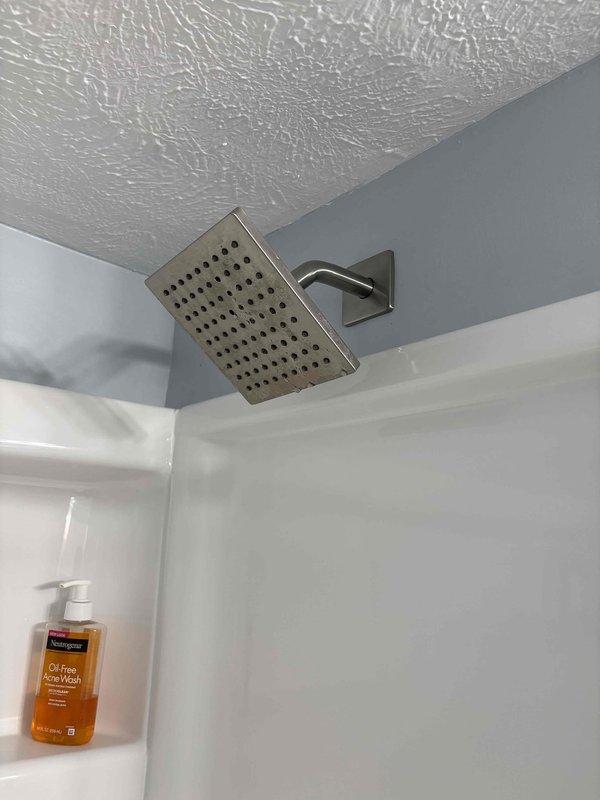 Completed estimate for replacement of 12-year-old residential water heater, with company to supply and install new unit. Assessment included installation of customer-supplied rainfall showerheads in bathroom with marble-effect tile surround. Documented existing bathroom fixtures featuring brushed nickel rectangular rainfall showerhead mounted via angular wall arm, contemporary tile work in beige and taupe tones with natural veining patterns installed in horizontal brick-lay pattern, and two-tone wall paint scheme. Photographed installation areas to document current conditions and fixture specifications for replacement planning purposes.