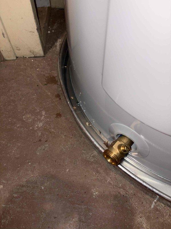 Responded to water heater leak on a 2-year-old unit under warranty. Upon inspection, found significant corrosion and rust at the base of the tank where the white exterior meets the metal rim, with visible deterioration around the drain valve assembly. The leak originated from the compromised tank base, evidenced by floor staining and water damage on the concrete surface beneath the unit. Due to the extent of tank corrosion and active leaking from the base, recommended full water heater replacement as the tank integrity has been compromised beyond repair.