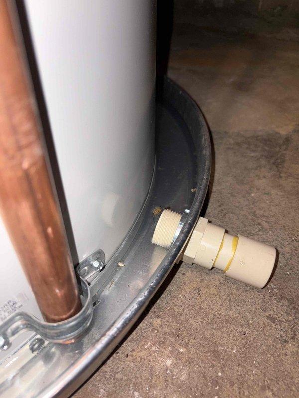 Responded to water heater leak on a 2-year-old unit under warranty. Upon inspection, found significant corrosion and rust at the base of the tank where the white exterior meets the metal rim, with visible deterioration around the drain valve assembly. The leak originated from the compromised tank base, evidenced by floor staining and water damage on the concrete surface beneath the unit. Due to the extent of tank corrosion and active leaking from the base, recommended full water heater replacement as the tank integrity has been compromised beyond repair.