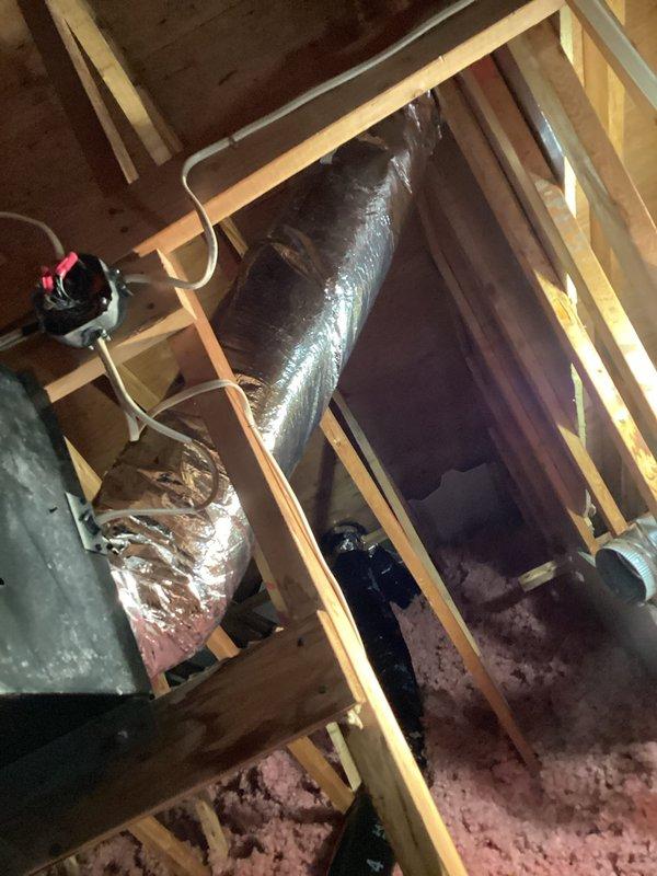 Insulated bathroom exhaust ductwork in attic space to prevent heat loss and condensation issues. Wrapped flexible black exhaust duct with appropriate insulation material and secured metallic silver flexible ducts running through attic joists, ensuring proper support and thermal efficiency throughout the ventilation system.