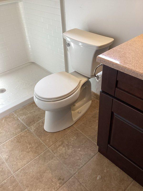 Completed installation of walk-in shower system including white subway tile walls in brick-lay pattern, molded shower pan with center drain, chrome shower head assembly, and horizontal chrome grab bar for safety. All plumbing fixtures installed and operational, with proper water supply connections and drainage completed per code requirements.