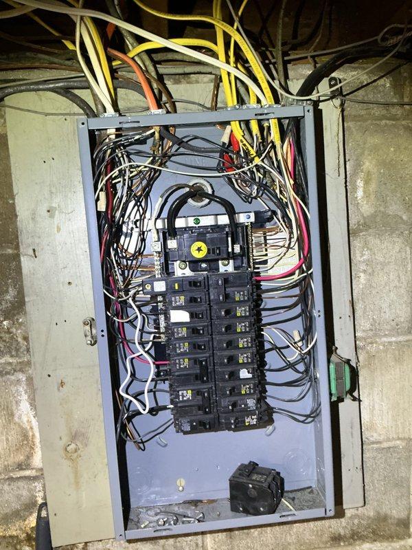 Conducted comprehensive electrical assessment for proposed electrical service upgrade and transfer switch installation. Evaluated existing electrical panel configuration, which currently houses two vertical columns of circuit breakers with main disconnect at top of enclosure. Documented complex wiring arrangement with multiple circuits entering panel from above, including various gauge conductors in standard color coding. Assessed current panel capacity, breaker arrangement, and existing circuit distribution to determine scope of upgrade work required.

Inspected structural mounting conditions on concrete block foundation wall and evaluated available space for transfer switch installation. Photographed existing electrical infrastructure, including wire routing through ceiling joists, proximity to HVAC systems and other utilities, and overall condition of current installation. Prepared detailed electrical estimate covering service upgrade specifications and transfer switch integration r