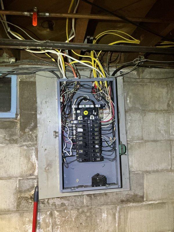Conducted comprehensive electrical assessment for proposed electrical service upgrade and transfer switch installation. Evaluated existing electrical panel configuration, which currently houses two vertical columns of circuit breakers with main disconnect at top of enclosure. Documented complex wiring arrangement with multiple circuits entering panel from above, including various gauge conductors in standard color coding. Assessed current panel capacity, breaker arrangement, and existing circuit distribution to determine scope of upgrade work required.

Inspected structural mounting conditions on concrete block foundation wall and evaluated available space for transfer switch installation. Photographed existing electrical infrastructure, including wire routing through ceiling joists, proximity to HVAC systems and other utilities, and overall condition of current installation. Prepared detailed electrical estimate covering service upgrade specifications and transfer switch integration r