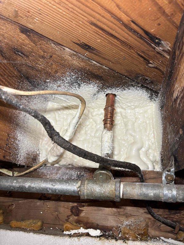 Responded to service call for reported boiler leak on 1-year-old Utica WT 2-2030 unit. Upon inspection, located leak source at corroded pipe connection in crawl space area adjacent to boiler installation. Identified moisture damage and discoloration on surrounding wooden framing members and compromised fiberglass insulation from water exposure. Assessed threaded pipe connections and galvanized steel piping showing surface corrosion and deterioration. Documented conditions with photographs showing affected plumbing infrastructure, spray foam insulation areas, and copper piping with visible oxidation. Addressed leak at connection point and verified system integrity upon completion.