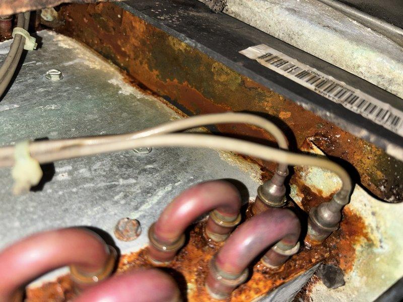 Completed annual cooling maintenance on 16-year-old Goodman system. Documented significant rust and corrosion on evaporator coil housing and air handler components, indicating prolonged moisture exposure and condensation issues. Refrigerant lines show discoloration but remain serviceable; however, extensive deterioration of metal framework and horizontal surfaces poses concern for system longevity and potential failure points.