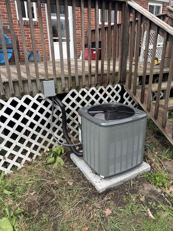 Completed full air conditioning system installation at residential property. Installed outdoor condenser unit on concrete pad in backyard area with proper refrigerant line connections and electrical conduit routing to building. Unit positioned adjacent to elevated wooden deck with decorative white lattice screening panels placed for equipment concealment. System tested and operational upon completion.