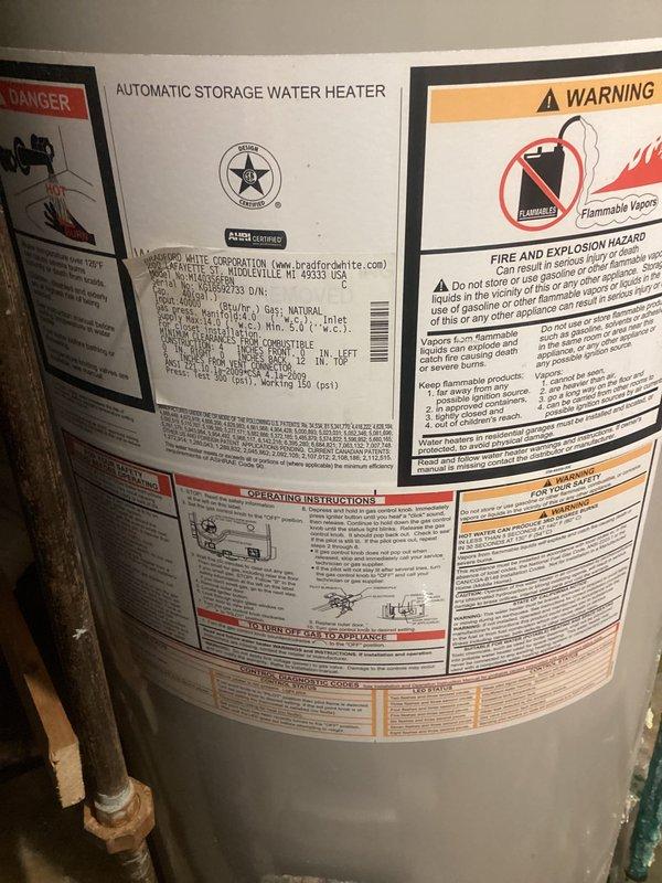 Conducted on-site evaluation of residential water heater system and documented current equipment condition. Inspection revealed an A.O. Smith automatic storage water heater with significant corrosion on pressure relief discharge piping, exhibiting green and white oxidation buildup and mineral deposits. Unit positioned in basement utility area with drain pan present beneath tank. Photographed manufacturer labels, safety warnings, AHRI certification markings, and all visible plumbing connections including copper supply lines and brass fittings at top of unit. Documented floor conditions showing water staining and mineral deposits around base of equipment, indicating potential historical discharge or seepage. Provided comprehensive estimate for water heater replacement options based on observed equipment age, corrosion severity, and current operating condition.