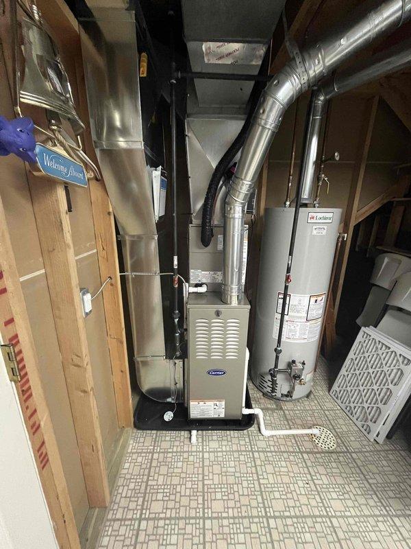 Completed full HVAC system installation including new Carrier furnace and outdoor condensing unit. Furnace installed in basement mechanical room with proper ductwork connections and ventilation, water heater clearances maintained per code. AC condenser positioned on concrete pad in backyard with electrical disconnect mounted to exterior wall, refrigerant lines and conduit properly secured to siding, unit placed on level foundation with adequate clearance for airflow and service access.