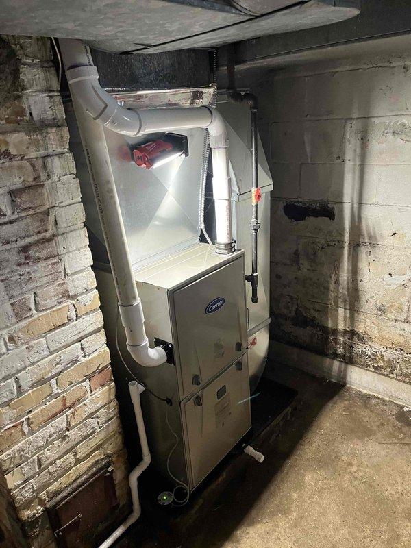 Completed full installation of Carrier brand furnace unit in basement utility space. System was mounted against masonry wall with proper clearances, connected to existing ductwork distribution system, and equipped with white PVC venting and condensate drainage piping routed vertically through ceiling. All gas line connections, electrical wiring, and safety controls were installed per manufacturer specifications and local code requirements, with system tested and verified operational upon completion.