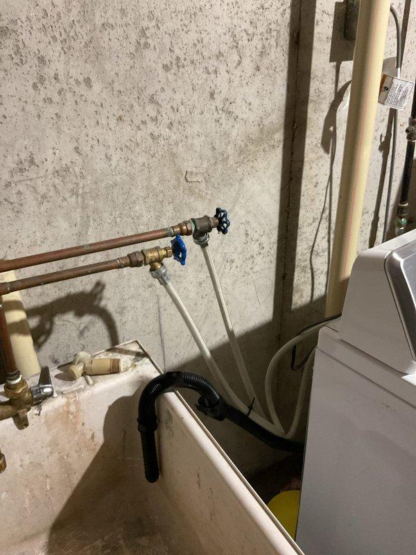 Responded to washing machine hot water supply line leak at connection point. Upon arrival, found the hot water hose connection to the washing machine actively dripping despite the shut-off valve being closed. Inspected the copper supply lines with shut-off valves (black and blue handled) and PEX connections in the utility area. Identified failed rubber washer and improper seal at the hose-to-machine connection as the source of the leak. Replaced the supply hose with new braided stainless steel washing machine connector, ensuring proper gasket installation and secure threading at both the valve outlet and machine inlet. Verified shut-off valves were functioning correctly and holding pressure when closed. Restored water supply and tested connections under full pressure to confirm leak was eliminated. Photographed existing plumbing infrastructure including copper supply lines, shut-off valves, and PEX tubing installation for service records. All connections secure with no active leaks upo