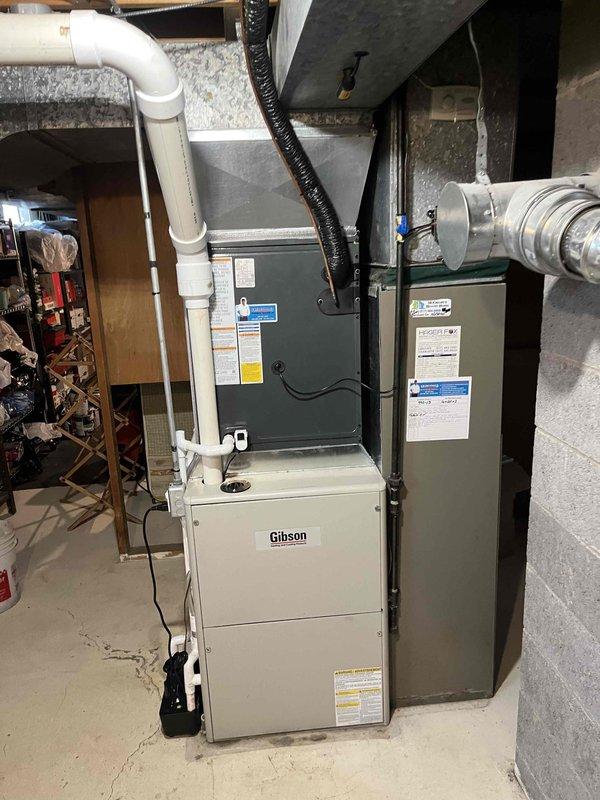 Completed full air conditioning system installation including indoor air handler and outdoor condensing unit. Indoor equipment installed in basement mechanical room with proper clearances, connected to existing furnace system, with PVC condensate drainage and venting properly routed. Outdoor condensing unit positioned on concrete pad adjacent to residence with electrical disconnect installed, refrigerant lines connected and charged, system tested and verified operational.