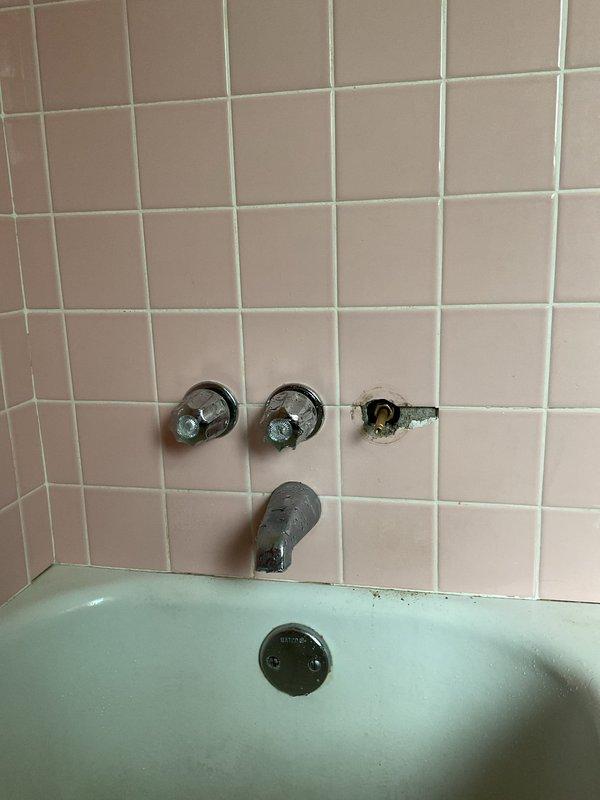 Responded to a quoted repair request for a deteriorating triple-handle shower valve assembly in a vintage bathroom with pink tile and mint green bathtub. Replaced the compromised right-side valve handle and trim, which exhibited exposed mounting hardware, damaged surrounding tile, and deteriorated grout and caulking. Restored proper function to the three-handle tub/shower configuration and addressed cosmetic damage to maintain water-tight integrity of the installation.