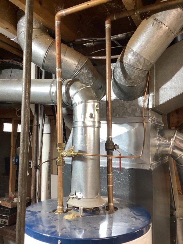 Responded to service call for leaking Envirotemp water heater with water accumulation present at base of unit for approximately three to four days. Upon inspection, confirmed active leak underneath water heater with visible water staining on concrete floor surrounding unit. Documented equipment condition with photographs showing copper plumbing connections, unit specifications, and extent of water damage in utility area.