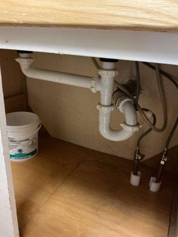 Responded to plumbing leak under kitchen sink. Upon arrival, inspected cabinet interior and identified leak source at P-trap assembly connections. Tightened loose fittings on white PVC P-trap where drain pipes connect to eliminate water seepage. Verified water supply lines and connections were secure and functioning properly. Tested system by running water through sink to confirm leak was resolved and all drain connections remained dry under normal flow conditions.