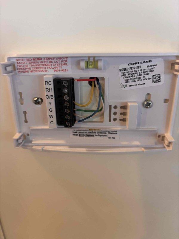Responded to service call for malfunctioning 13-year-old Emerson digital thermostat. Upon inspection, confirmed thermostat failure while HVAC system retained heating and cooling capabilities. Documented existing wiring configuration at terminal block showing proper connections at RC, RH, O/B, Y, G, and W/C terminals with red, yellow, green, and blue wires. Removed failed Emerson thermostat from wall mount and photographed unit and wiring for service records. System operational with heating and cooling functions intact despite thermostat display issues.