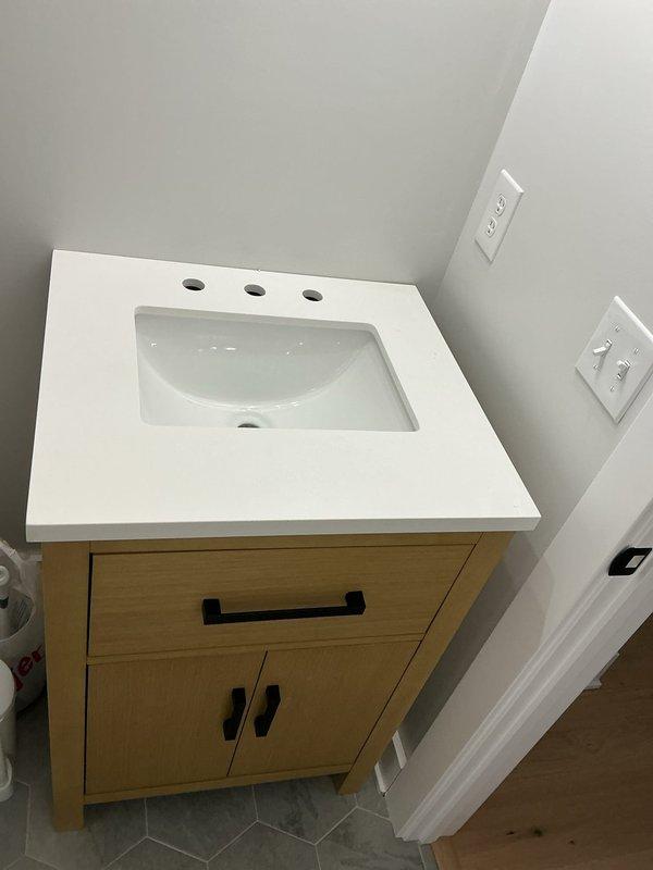 Replaced two outdated sink fixtures in separate areas of the residence with new vanity and plumbing connections. Successfully installed bathroom vanity unit with integrated white countertop sink basin, light wood cabinetry, and completed all water supply and drain line connections to ensure proper functionality.