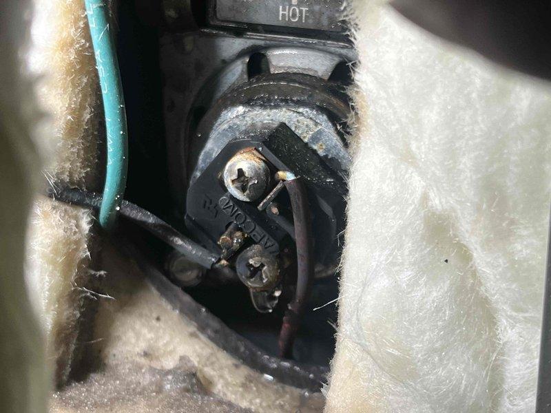 Responded to repeat water leak issue on residential water heater unit installed approximately two years ago with warranty expiring October 2033. Upon inspection, identified active leak at water heater connections and documented condition of unit and surrounding utility area including HVAC equipment and copper piping. Photographed electrical connections showing signs of age and corrosion at hot wire terminal within insulated cavity, as well as overall installation setup with visible plumbing connections, drain location, and equipment placement to assess potential water damage and determine appropriate repair or replacement recommendation.