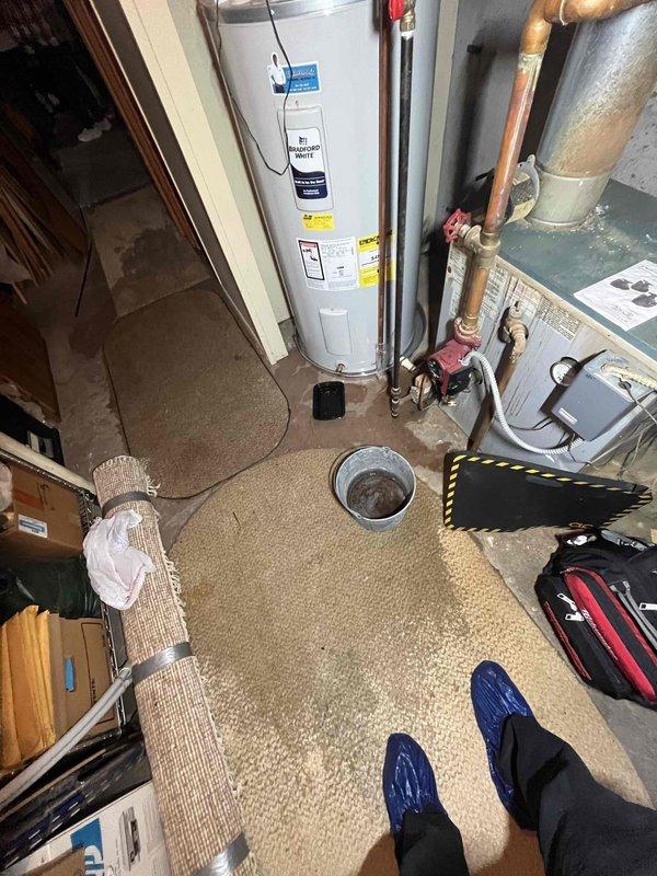 Responded to repeat water leak issue on residential water heater unit installed approximately two years ago with warranty expiring October 2033. Upon inspection, identified active leak at water heater connections and documented condition of unit and surrounding utility area including HVAC equipment and copper piping. Photographed electrical connections showing signs of age and corrosion at hot wire terminal within insulated cavity, as well as overall installation setup with visible plumbing connections, drain location, and equipment placement to assess potential water damage and determine appropriate repair or replacement recommendation.