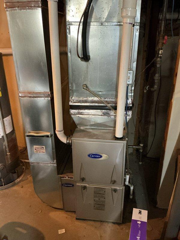 # CP-Cooling Problem

Responded to no-cooling complaint on 16-year-old residential air conditioning system originally installed in 1998. Customer reported indoor fan operating normally but outdoor condensing unit failing to start. Upon arrival, performed visual inspection of outdoor unit and indoor furnace/air handler assembly. Photographed equipment condition showing Carrier furnace with associated ductwork and outdoor condensing unit location. Outdoor unit displayed significant weathering, vegetation growth, and deteriorated piping connections with visible corrosion at refrigerant line joints. System showed age-related wear consistent with equipment nearing end of expected service life. Diagnosed failed outdoor unit preventing normal cooling operation while blower motor continued functioning independently. Documented findings with photos of basement mechanical equipment and exterior condensing unit area for service records.