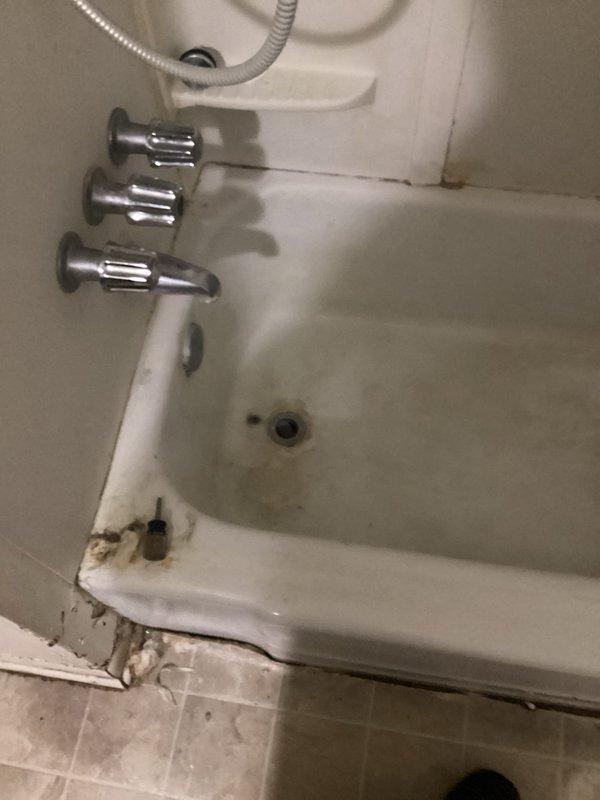 # Plumbing Leak Repair - Shower Head

Responded to service call for leaking shower head in bathroom. Upon arrival, inspected the three-handle chrome faucet system and handheld shower assembly mounted above bathtub. Identified active leak at shower head connection point. 

Assessment revealed significant water damage and deterioration at tub base and adjacent wall trim, with rust staining, corrosion, and peeling material indicating prolonged moisture exposure. The compromised condition of the bathtub edge and surrounding floor area suggested the leak had been present for an extended period.

Addressed the leaking shower head by inspecting connection points, seals, and mounting hardware. Completed necessary repairs to stop active water leak and restore proper function to the shower system. Documented existing water damage to bathroom fixtures and structural elements for reference. Advised that additional restoration work may be needed to address the deteriorated tub base, damaged wall tr