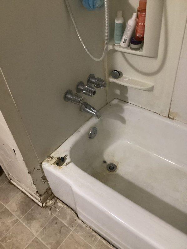 # Plumbing Leak Repair - Shower Head

Responded to service call for leaking shower head in bathroom. Upon arrival, inspected the three-handle chrome faucet system and handheld shower assembly mounted above bathtub. Identified active leak at shower head connection point. 

Assessment revealed significant water damage and deterioration at tub base and adjacent wall trim, with rust staining, corrosion, and peeling material indicating prolonged moisture exposure. The compromised condition of the bathtub edge and surrounding floor area suggested the leak had been present for an extended period.

Addressed the leaking shower head by inspecting connection points, seals, and mounting hardware. Completed necessary repairs to stop active water leak and restore proper function to the shower system. Documented existing water damage to bathroom fixtures and structural elements for reference. Advised that additional restoration work may be needed to address the deteriorated tub base, damaged wall tr