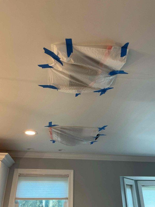 Responded to report of water spotting on second-floor ceiling with suspected leak from upstairs bathrooms. Cut two access openings in ceiling to investigate moisture trapped between drywall and existing popcorn ceiling layers. Installed temporary plastic containment barriers secured with painter's tape at both openings to prevent debris contamination. Exposed and inspected copper plumbing lines running through ceiling cavity, identifying multiple pipe runs servicing two full bathrooms above. Documented conditions with photographs showing plumbing configuration and ceiling structure for further assessment and repair planning.