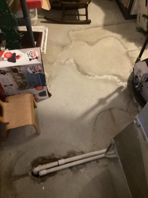 Responded to report of furnace leaking from pipe near unit, with leak active for three days in nineteen-year-old home. Upon arrival, inspected HVAC system and discovered condensate drainage issue causing water accumulation. Found black plastic condensate drip pan positioned beneath furnace unit containing standing water with visible mineral deposits and debris, indicating ongoing drainage problem. 

Investigated further and identified compromised condensate drain line system. Removed displaced insulation material from basement floor area surrounding furnace to access plumbing components and assess extent of water damage. Examined white PVC condensate drain piping with U-shaped trap configuration for blockages or improper pitch. Located source of leak at condensate drain connection point near furnace cabinet.

Cleared condensate line obstruction and verified proper drainage flow through system. Repositioned and secured drain pan to ensure adequate water collection capacity. Tested conde