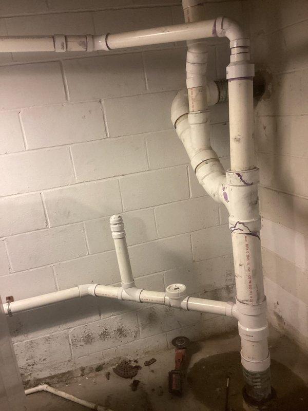 Completed plumbing project to integrate laundry drainage system into existing drain stack and install new sump pump system with excavated crock pit. Installed white PVC drainage piping with proper venting, including vertical stack connections and horizontal branch lines with appropriate fittings and elbow joints. Cut concrete floor and excavated pit for new sump crock installation. All pipe joints primed and cemented per code requirements. Two-day installation completed with proper drainage configuration to manage basement water collection and laundry waste water discharge.