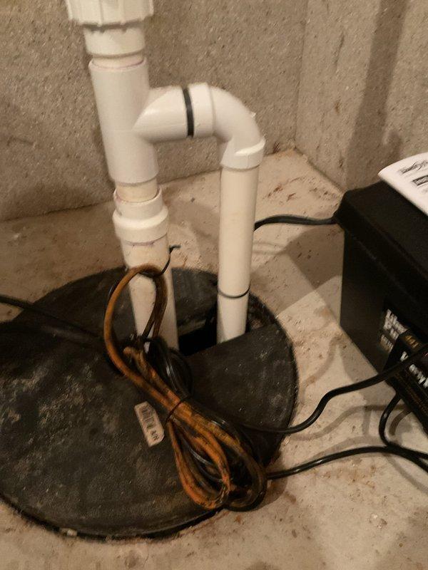 Installed battery backup system for existing sump pump in basement utility area. Connected backup power supply unit to sump pump basin assembly with proper electrical wiring secured along concrete block wall, ensuring system will maintain operation during power outages. Verified all PVC discharge piping connections and tested system functionality upon completion.