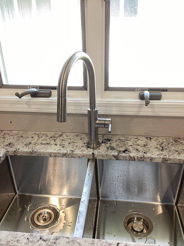 Completed installation of new kitchen plumbing fixtures including double-basin stainless steel sink with modern brushed stainless steel high-arc faucet, garbage disposal unit, and dishwasher connections. All plumbing connections secured with proper PVC drainage piping and supply lines installed per code, with system tested and verified leak-free upon completion.