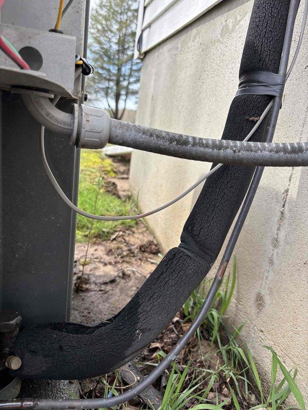 Completed annual heating and cooling maintenance visit including furnace and air conditioning tune-ups for a system without humidifier. Inspected electrical connections, refrigerant line fittings, and service ports on outdoor condensing unit, verifying all components were secure and functioning properly. Documented equipment condition with photos showing exterior service panel connections, refrigerant lines with insulation, and line set installation along building exterior.