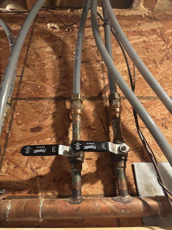 Responded to service call for leaking boiler pipes in crawl space. Upon inspection, identified active water leaks at copper manifold distribution system with corroded fittings and compromised connections to PEX supply lines. Found significant water staining on OSB subflooring around manifold area, indicating ongoing moisture intrusion. Assessed condition of black-handled ball valves and brass fittings showing oxidation and green patina from age and water exposure. Documented existing plumbing configuration including multiple PEX pipe runs connected to central copper manifold system. Photographed affected areas showing water damage, corroded components, and overall system layout for service records. Work completed per AMS authorization with no charge to customer.