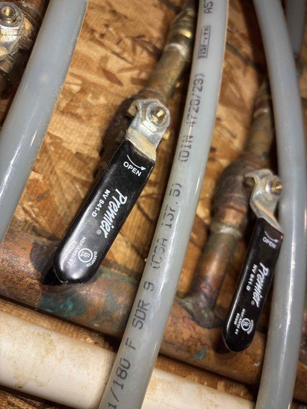Responded to service call for leaking boiler pipes in crawl space. Upon inspection, identified active water leaks at copper manifold distribution system with corroded fittings and compromised connections to PEX supply lines. Found significant water staining on OSB subflooring around manifold area, indicating ongoing moisture intrusion. Assessed condition of black-handled ball valves and brass fittings showing oxidation and green patina from age and water exposure. Documented existing plumbing configuration including multiple PEX pipe runs connected to central copper manifold system. Photographed affected areas showing water damage, corroded components, and overall system layout for service records. Work completed per AMS authorization with no charge to customer.